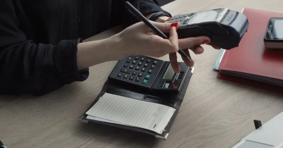 A business owner reviewing payment processing notes and a calculator beside a card terminal